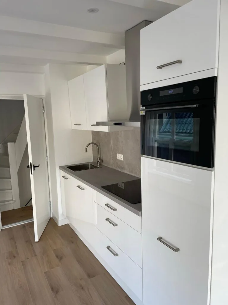Moderne witte keuken aan de Korte Kolksteeg met ingebouwde oven, inductiekookplaat en licht houten vloer.